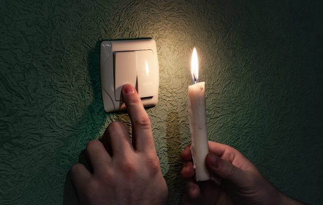 Holding burning candle in a dark room near a light switch, blackout. Power outage, energy crisis. Problems with power supply. Ukraine without power Holding burning candle in a dark room near a light switch, blackout. Power outage, energy crisis. Problems with power supply. Ukraine without power